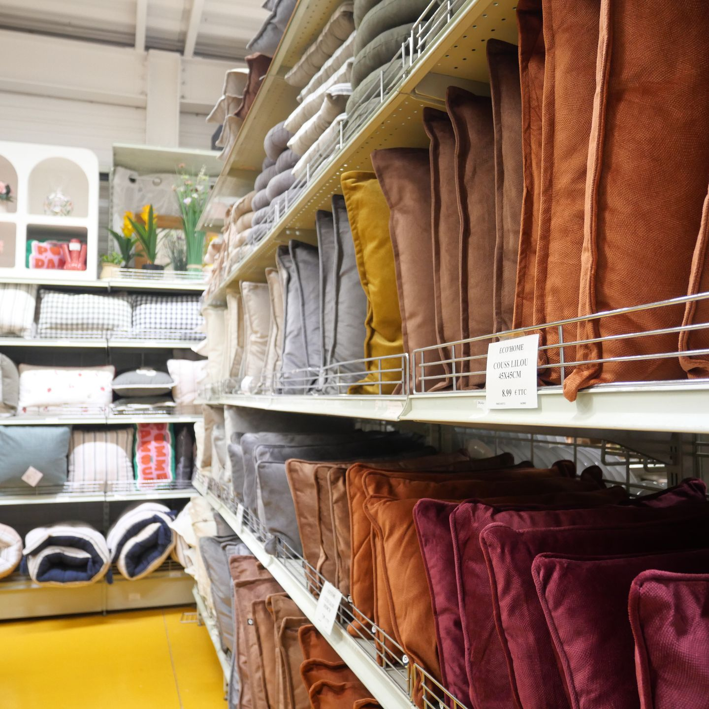 Des coussins empilés de couleur blanche, grise, beige et rouille sur des étagères métalliques.