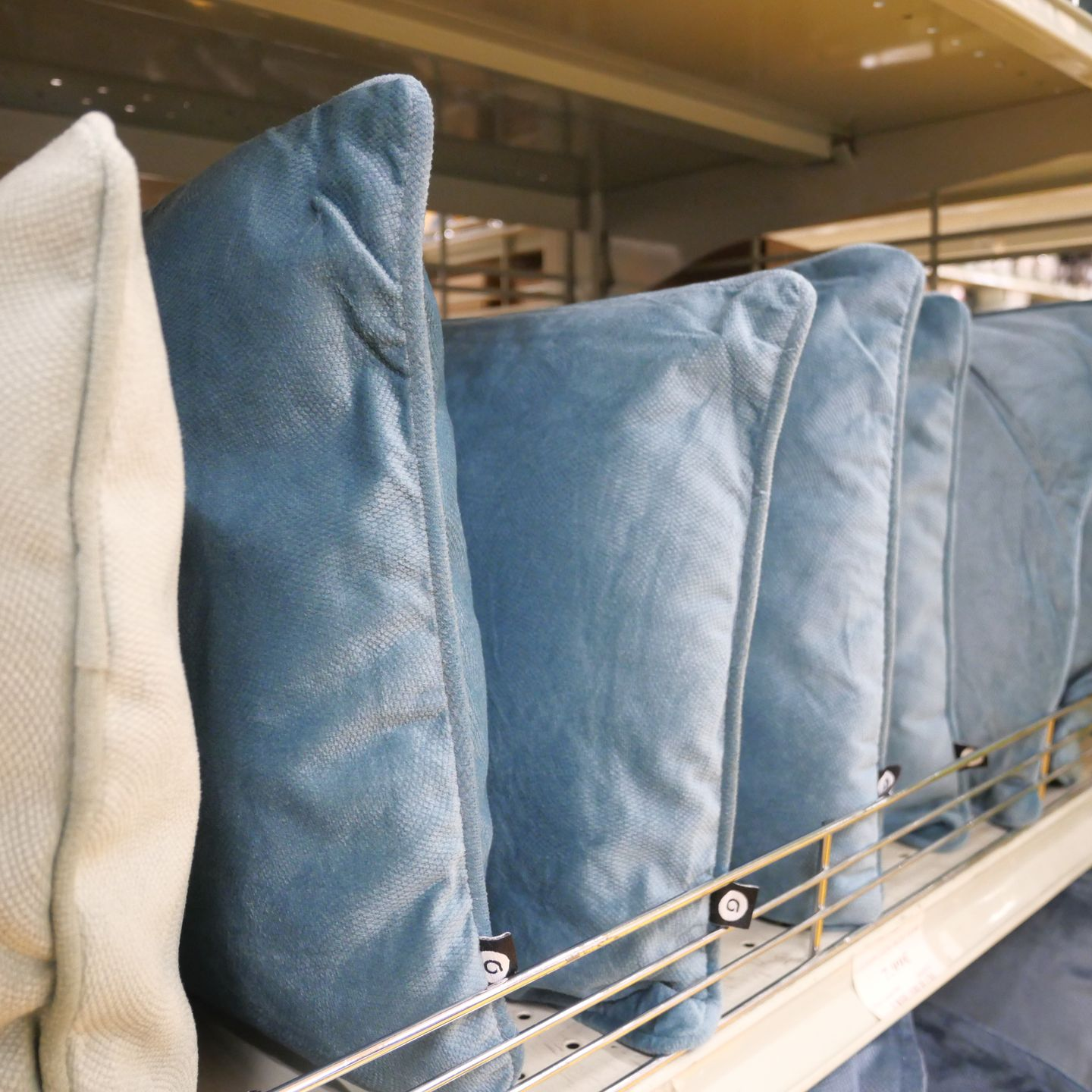 Des coussins bleus et crème alignés sur une étagère de magasin avec des rambardes métalliques.