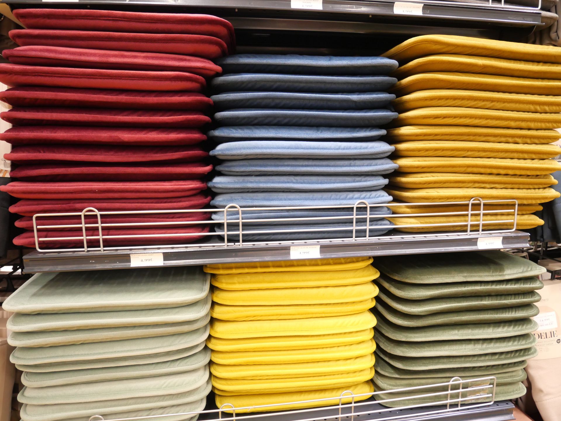 Des piles de coussins de siège rouges, bleus, jaunes et beiges sur les étagères du magasin.