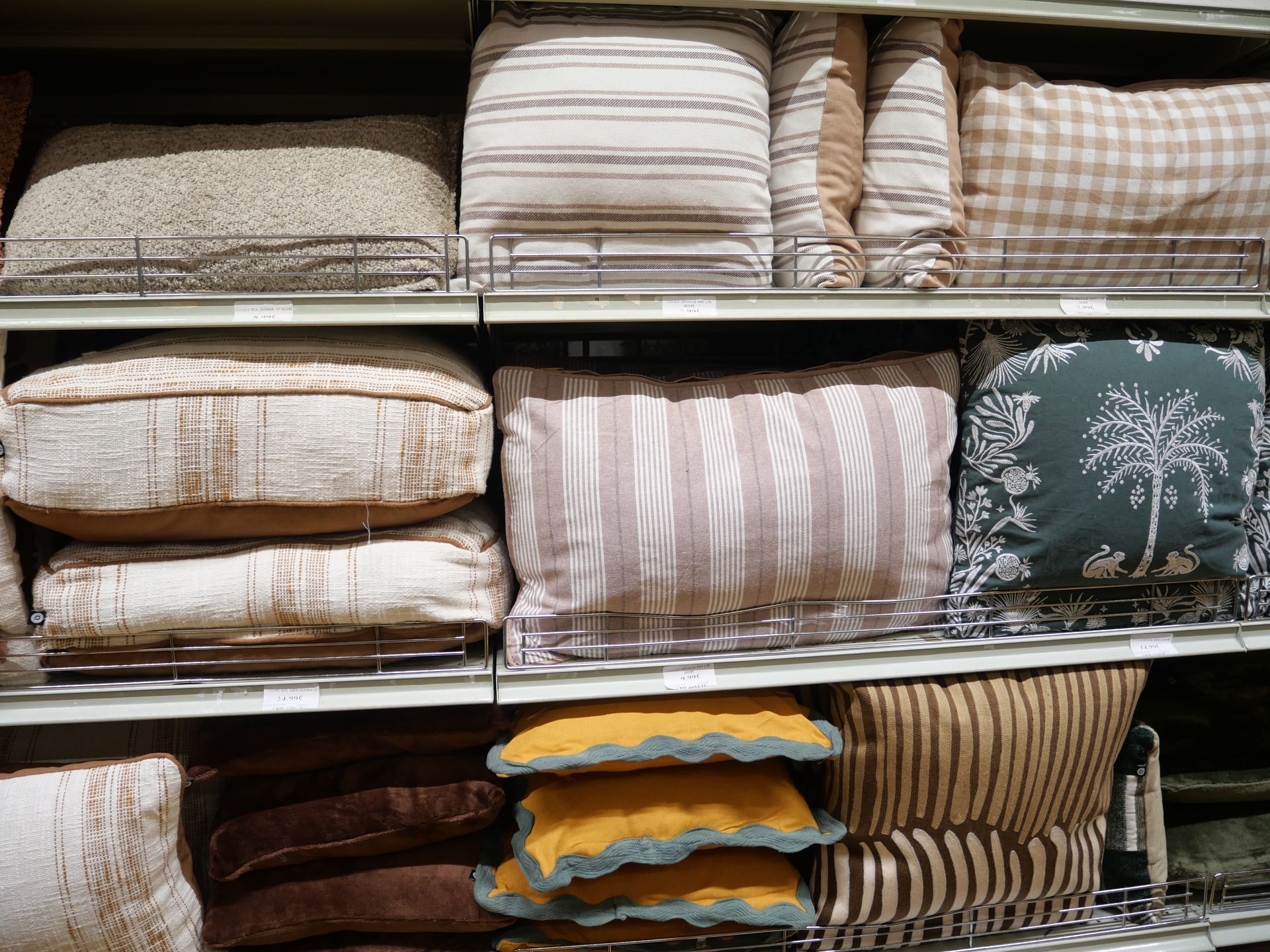 Des étagères remplies de coussins et d'oreillers à motifs, soigneusement pliés, dans les tons crème, beige, marron et vert.