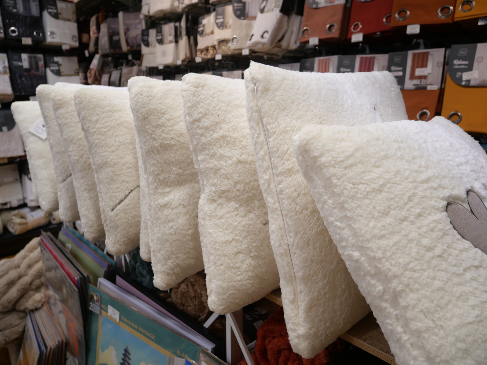 Une rangée de coussins blancs moelleux est exposée sur les étagères du magasin.