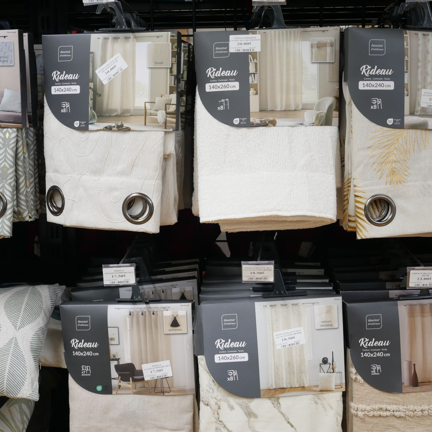 Rideaux présentés sur les étagères d'un magasin, principalement aux tons neutres beige, crème et gris, dans leurs emballages.
