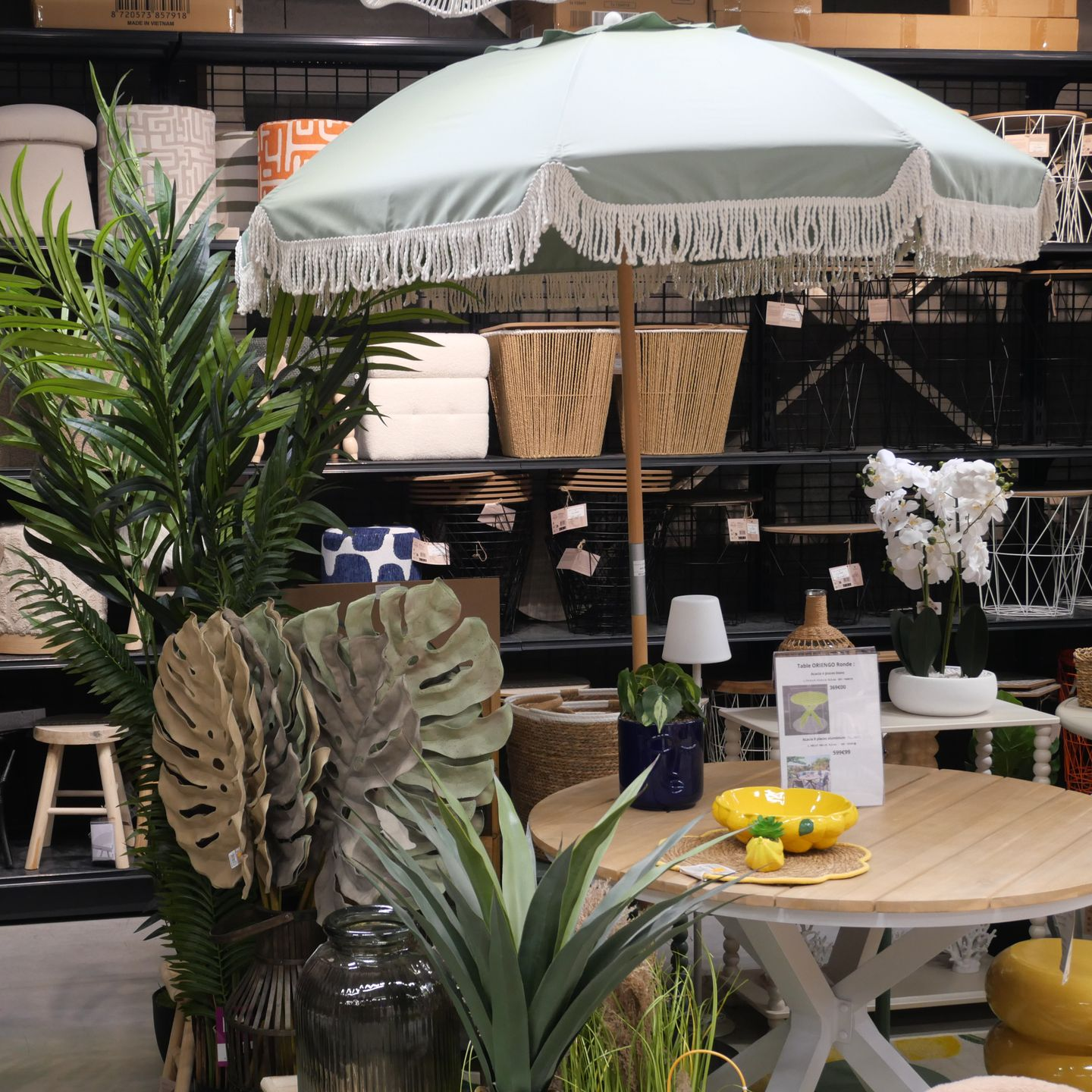 Parasol, table en bois, plantes et objets décoratifs au milieu des rayons d'un magasin.