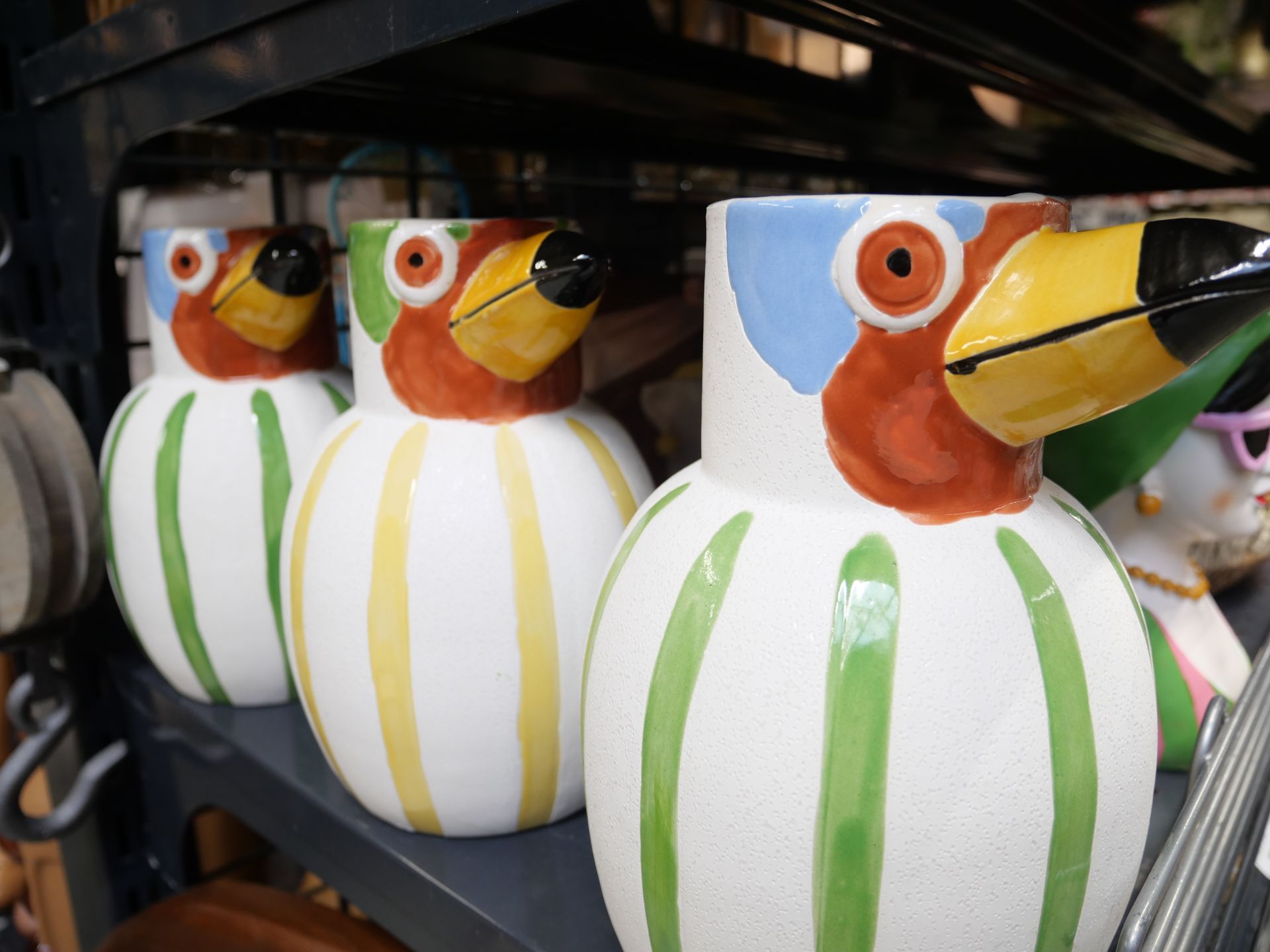 Des pots de fleurs en céramique colorés en forme d'oiseaux, à rayures blanches, empilés sur une étagère.
