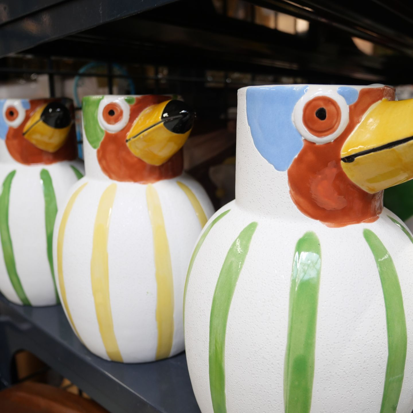 Vases en céramique peints en forme d'oiseau, avec des becs jaunes et des corps rayés jaunes et verts, sur une étagère.
