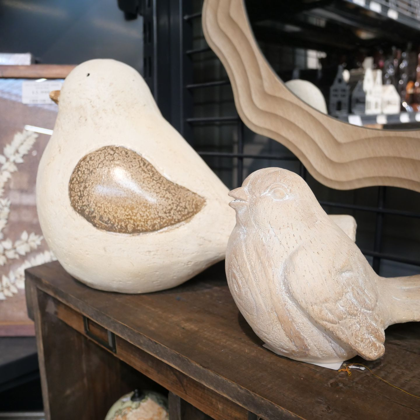 Deux sculptures d'oiseaux décoratives sur une table en bois, l'une couleur crème avec une aile.