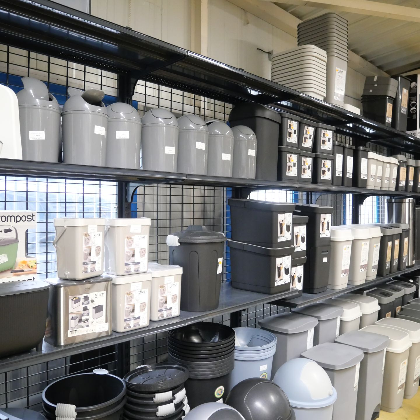 Des rayons de magasin remplis de bacs gris, de poubelles et de conteneurs en plastique.