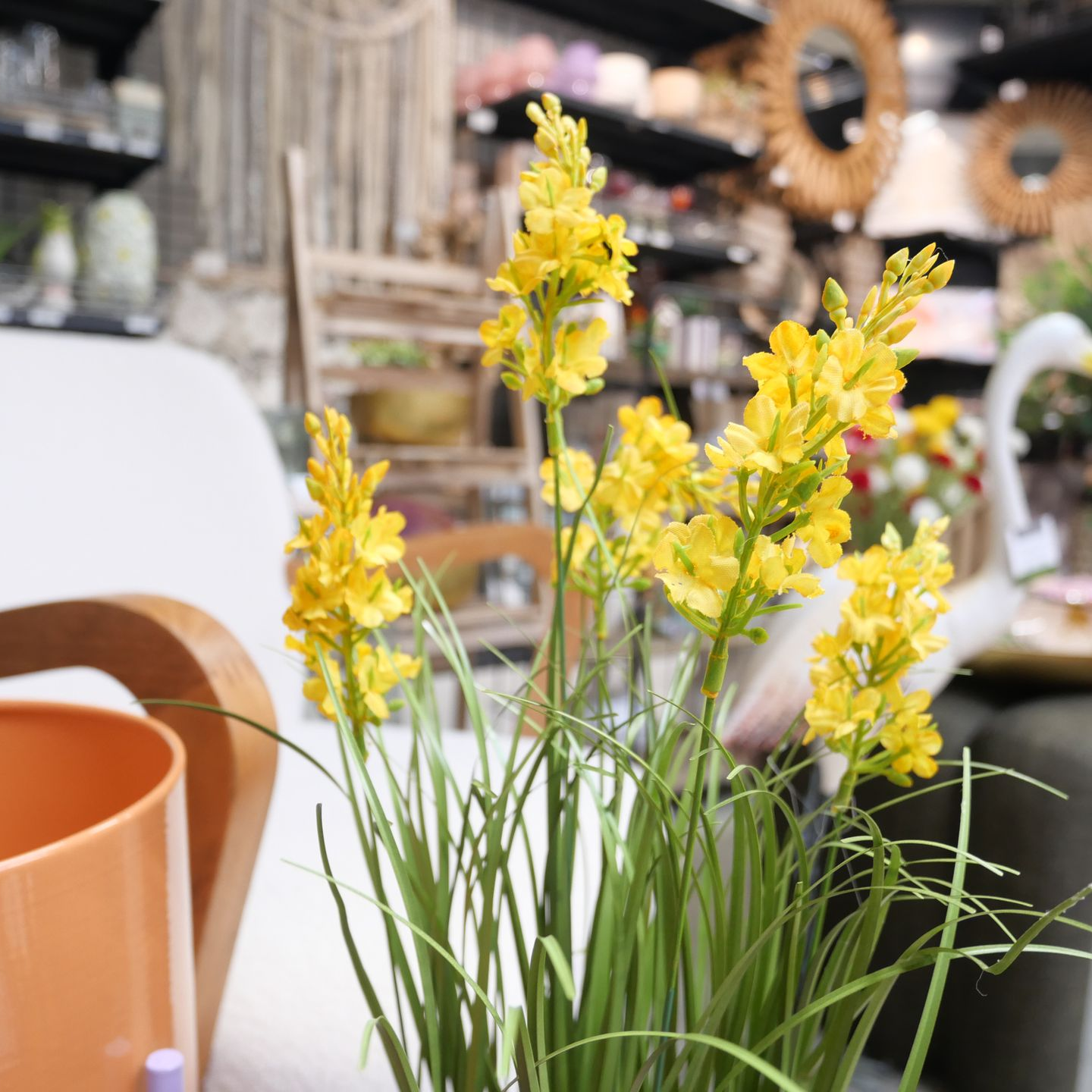 Des fleurs jaunes en pot sur une table, avec des tasses orange dans un rayon du magasin.