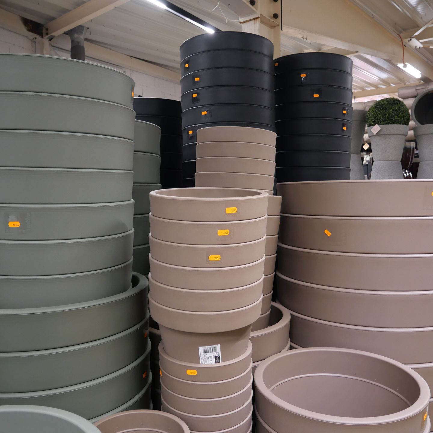 Des piles de grands pots de fleurs ronds gris, taupe et noirs sur les étagères du magasin.