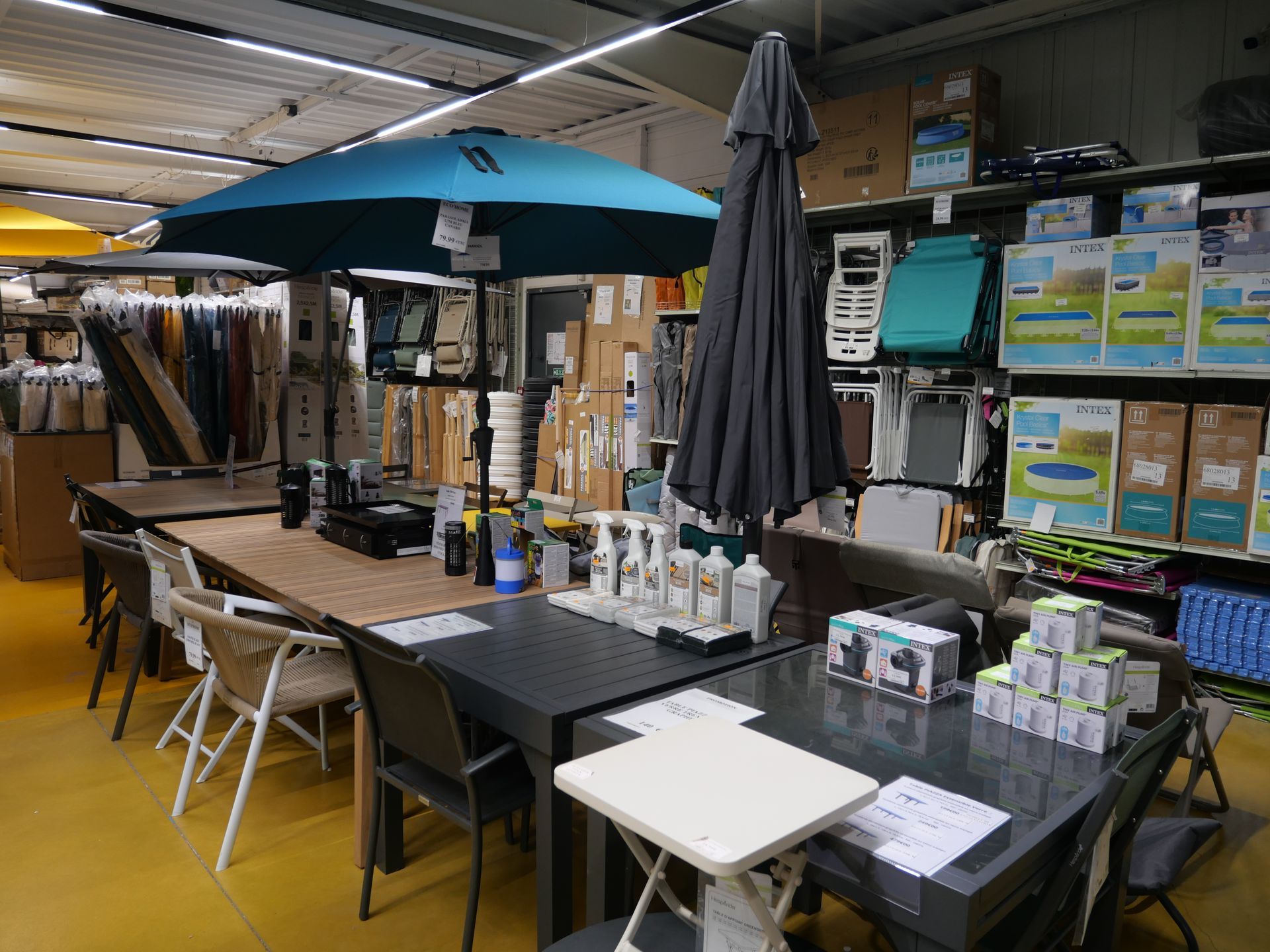 Mobilier d'extérieur avec tables, chaises et parasols dans une allée de magasin.