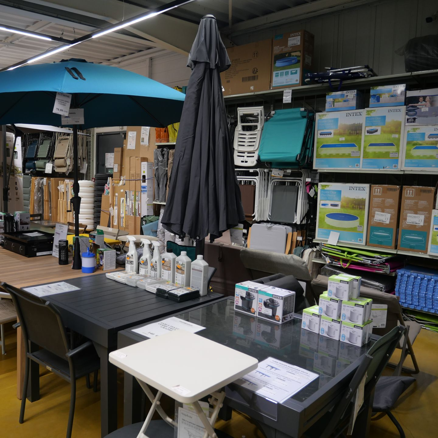 Chaises pliantes, tables, parasols et produits de piscine sur les étagères.