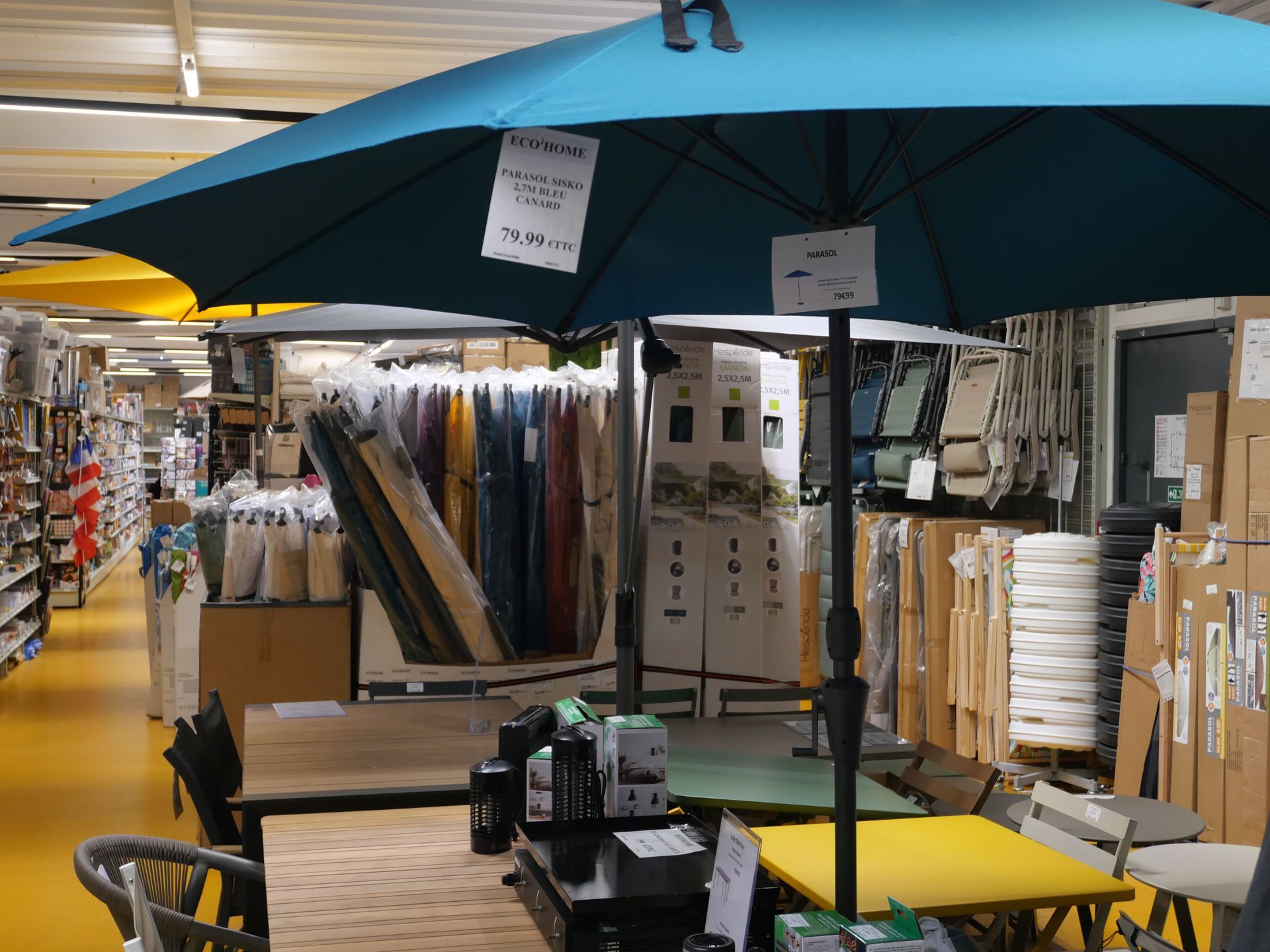 Grand parasol bleu, assortiment de coussins et d'accessoires de décoration d'extérieur.