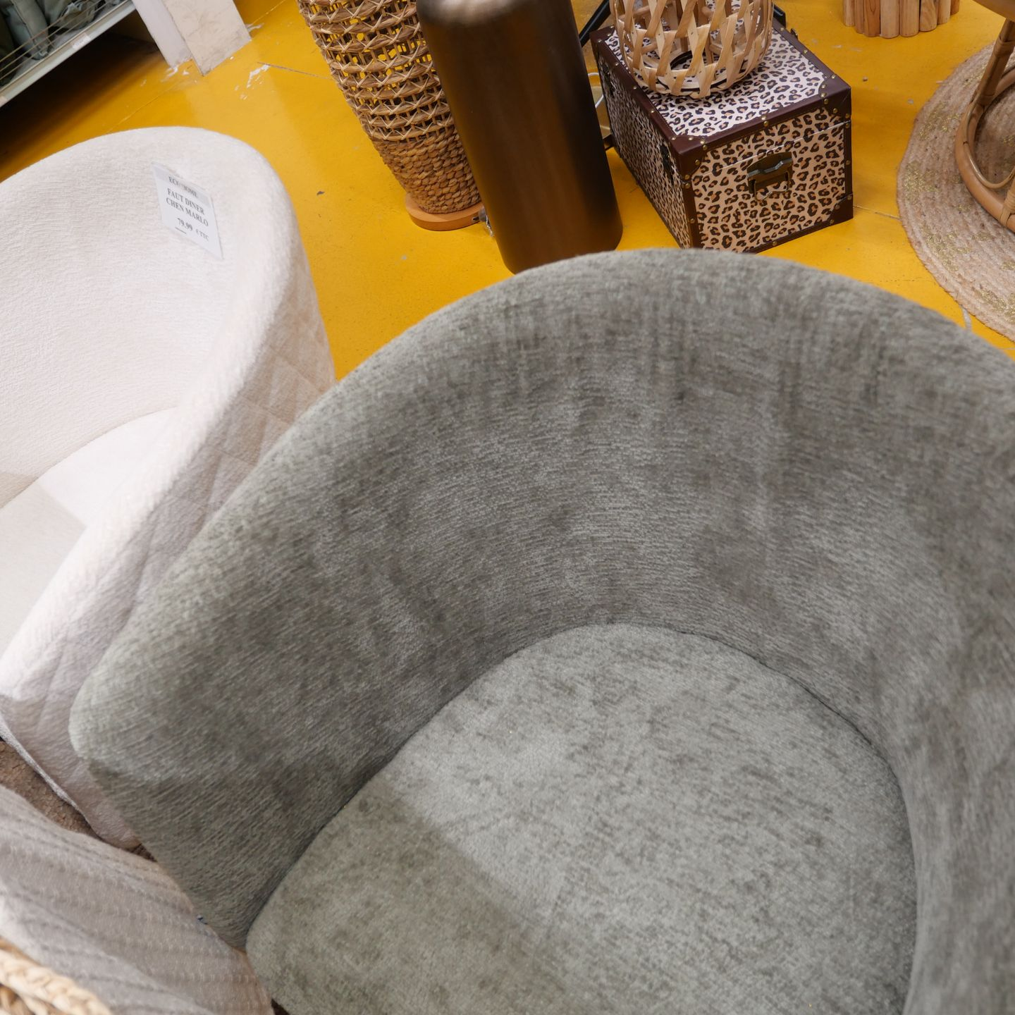 Au premier plan, un fauteuil gris capitonné, à côté d'une chaise blanche, sur un sol jaune.