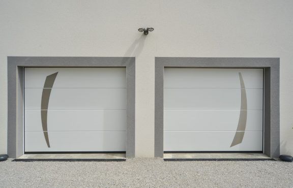 Deux portes de garage blanches aux accents gris incurvés, encadrées de gris, sur un mur clair.