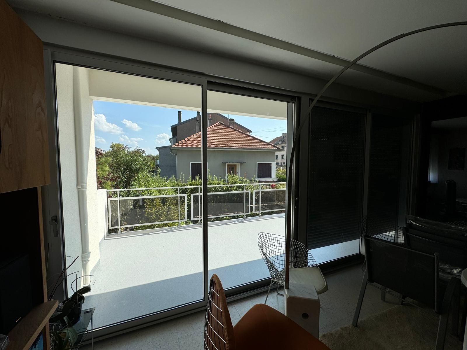 Des portes coulissantes en verre donnent sur un balcon et offrent une vue sur l'extérieur ; à l'intérieur, on trouve une plante en pot et une chaise.