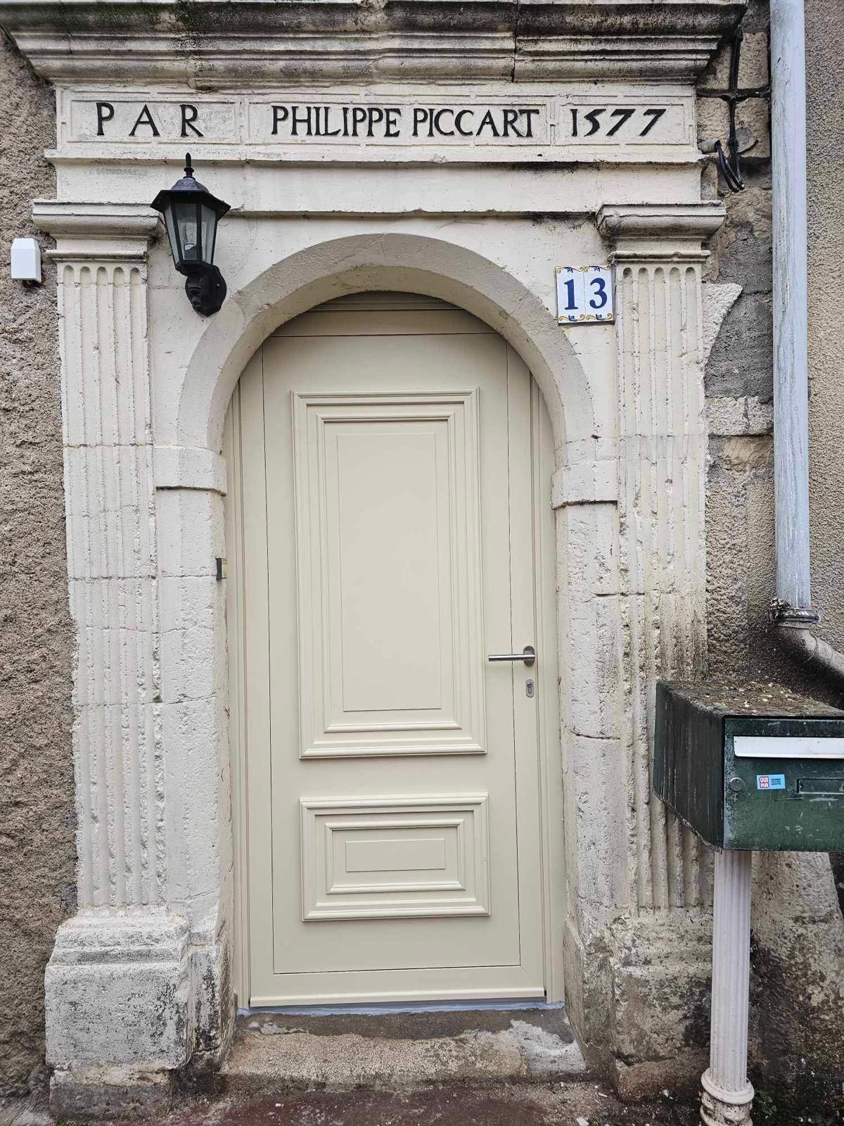 Porte en bois couleur crème avec cadre en pierre arquée, datée de 1577. « PAR PHILIPPE PICCART » au-dessus de la porte, numéro 13 sur le côté.