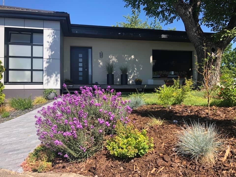 Porte blanche à panneaux de verre donnant sur une cour arrière avec de l'herbe verte et un ciel bleu partiellement nuageux.