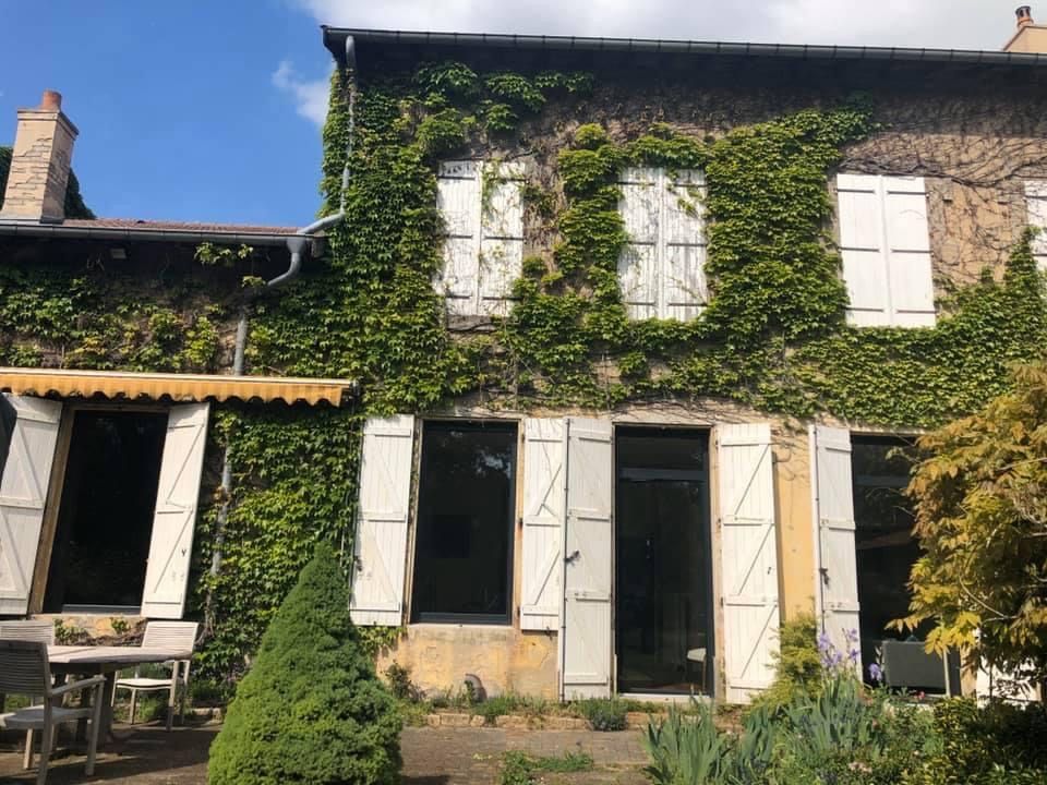 Extérieur d'une maison moderne avec une porte grise, une cheminée et une fenêtre de toit par une journée ensoleillée.