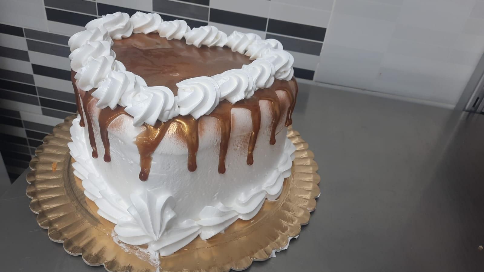 Pastel en forma de corazón con glaseado blanco, llovizna de chocolate y borde decorativo de glaseado blanco 