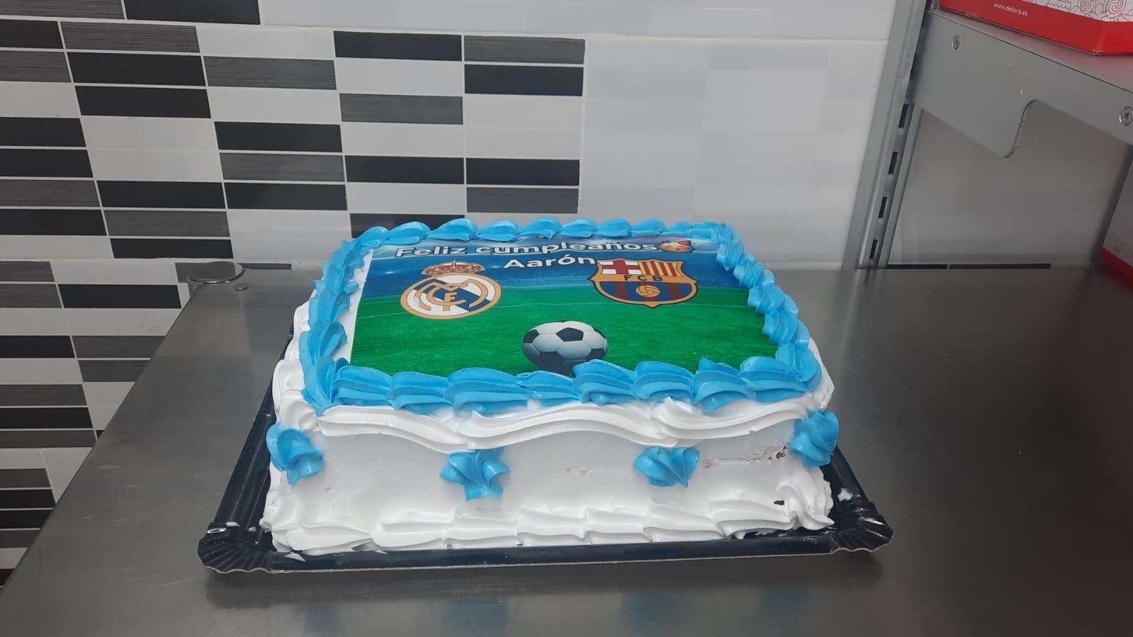 Pastel decorado con un campo de fútbol y logos de equipos, glaseado azul y blanco.