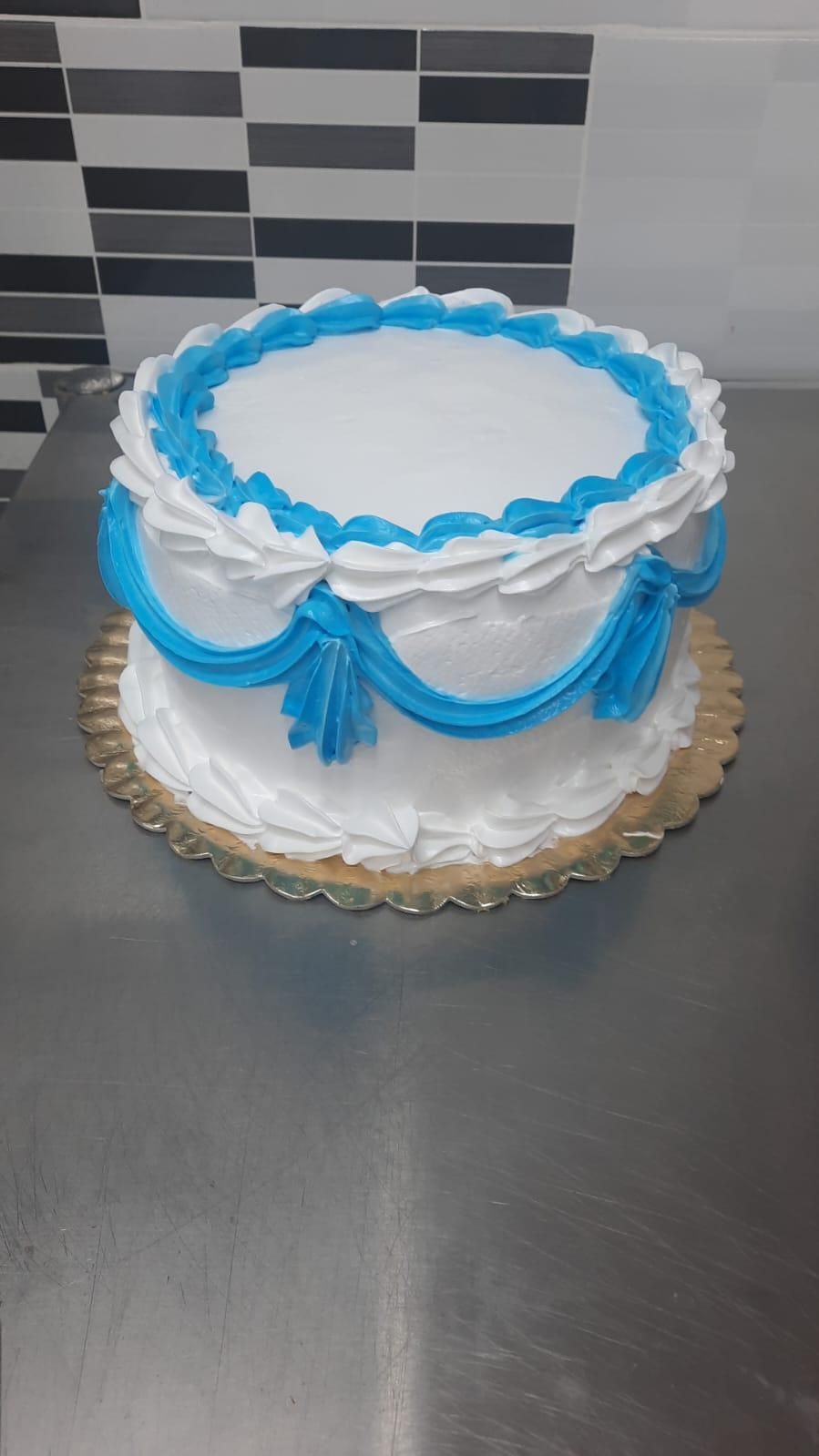 Pastel blanco con detalles de glaseado azul sobre una base de pastel dorada, colocada sobre una superficie