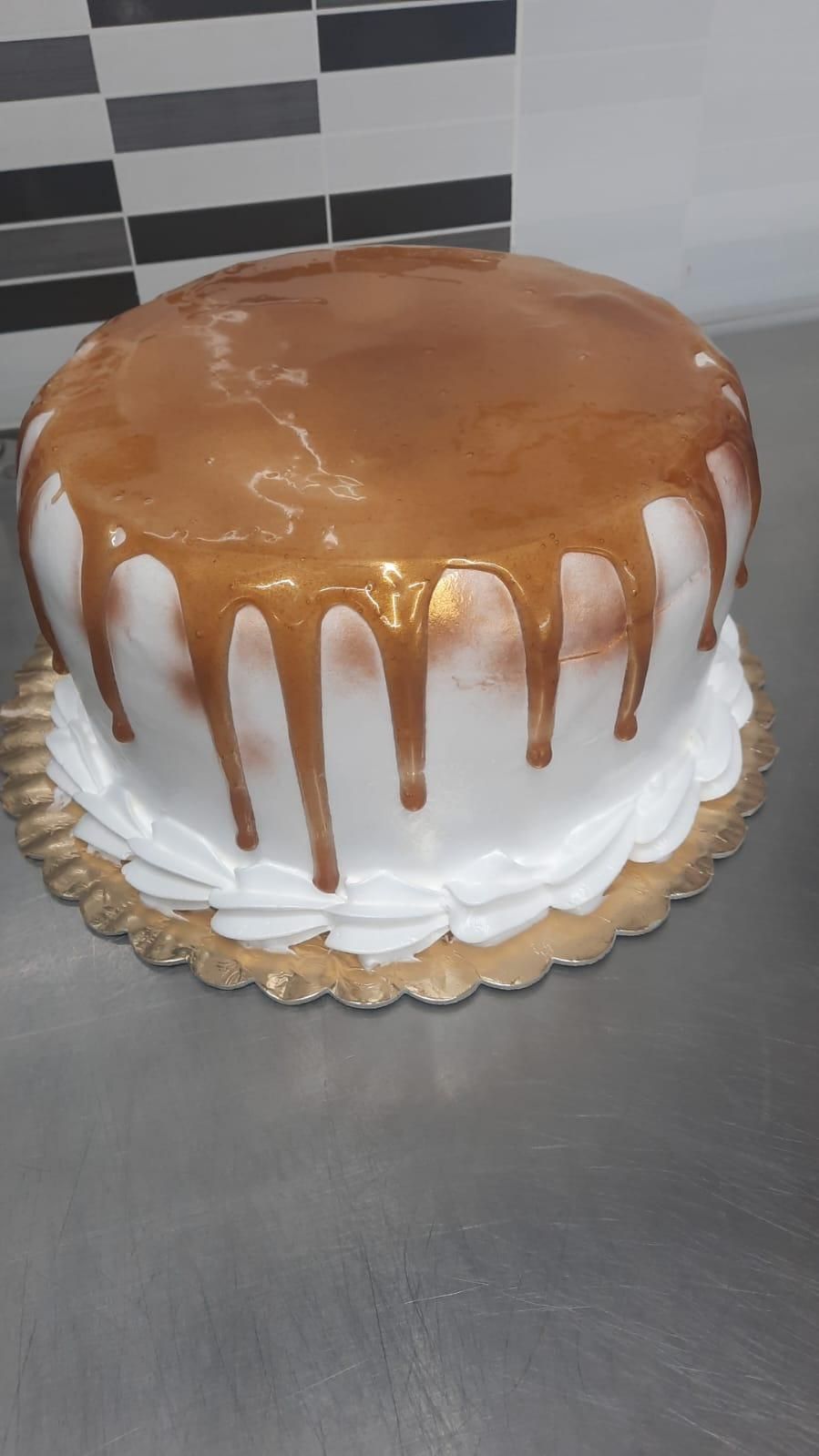 Pastel con glaseado blanco, glaseado de caramelo y borde de glaseado blanco en bandeja dorada.