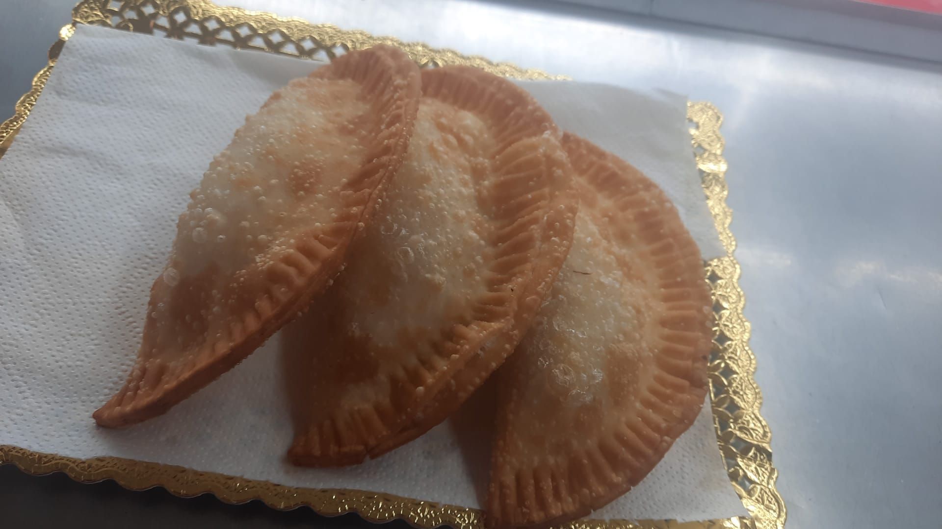 Tres pasteles dorados y fritos sobre una servilleta blanca, colocados en una bandeja decorativa.