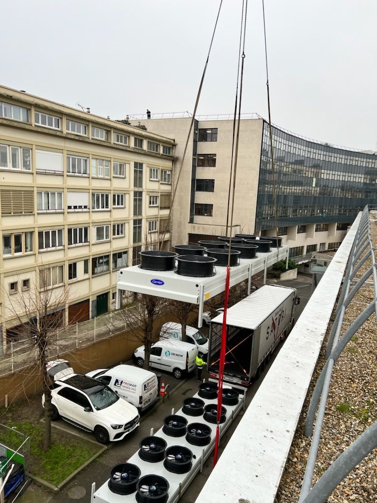 Pièce industrielle soulevée par une grue au dessus d'un parking
