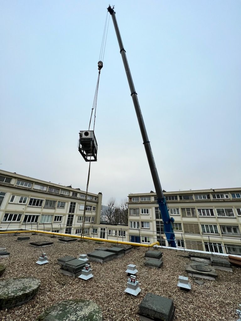 Pièce métallique soulevée en l'air par une grue en direction du toit d'un bâtiment