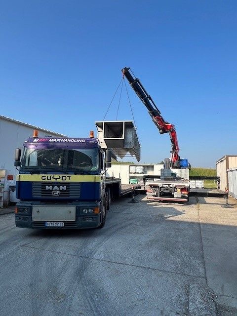 Bras de camion soulevant une pièce métallique au dessus d'un second camion