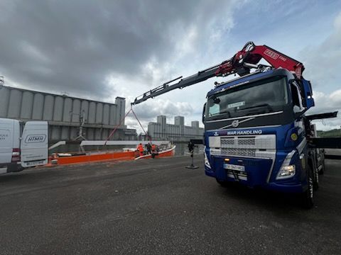 Camion bleu avec un bras de grue soulevant une poutre metallique