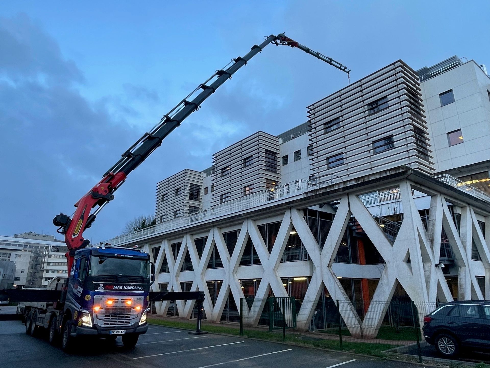 Camion bleu avec un bras de grue rouge qui soulève quelque chose au dessus d'un bâtiment