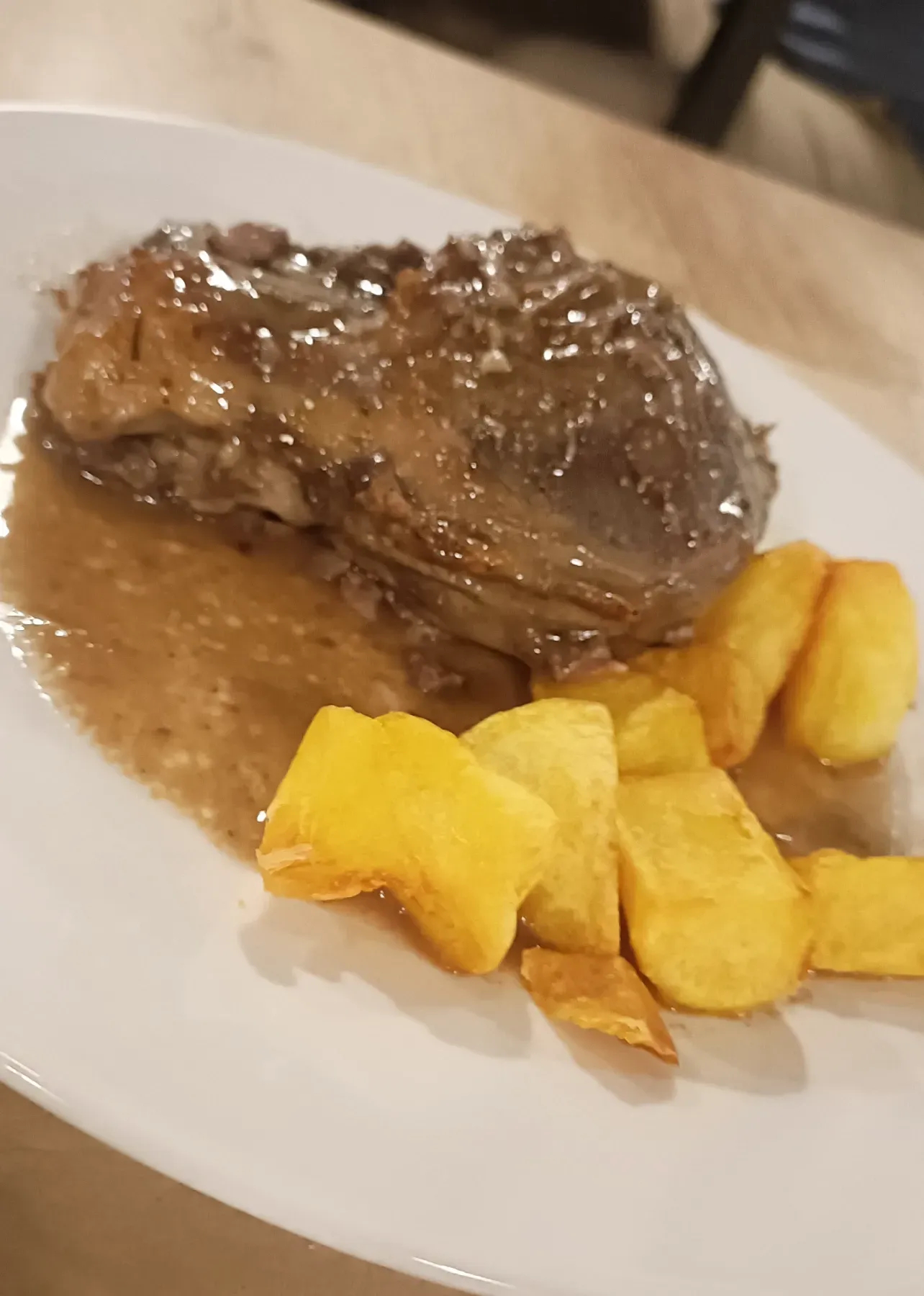 Plato de carne estofada con salsa, servido con patatas fritas doradas.