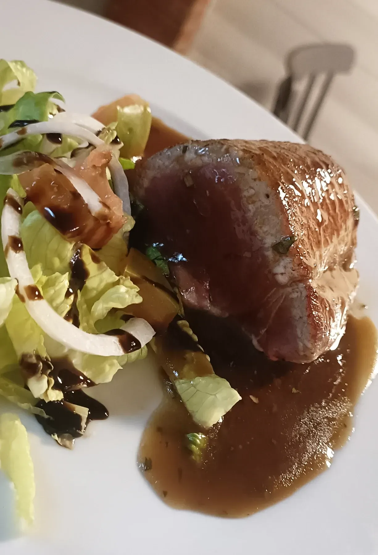 Bistec sellado con salsa marrón y ensalada con aros de cebolla, en un plato blanco.