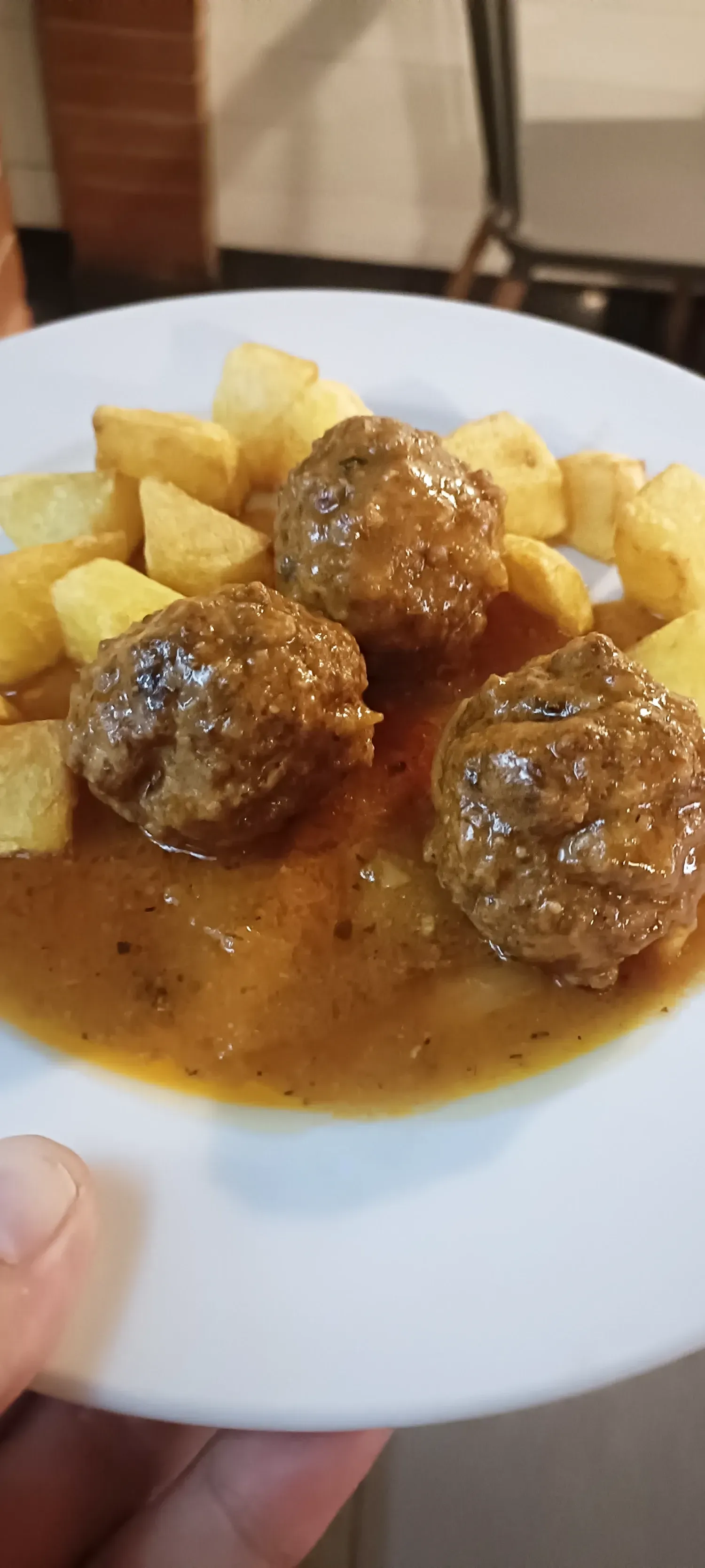 Albóndigas en salsa con patatas gajo en un plato blanco. Una mano sostiene el plato.