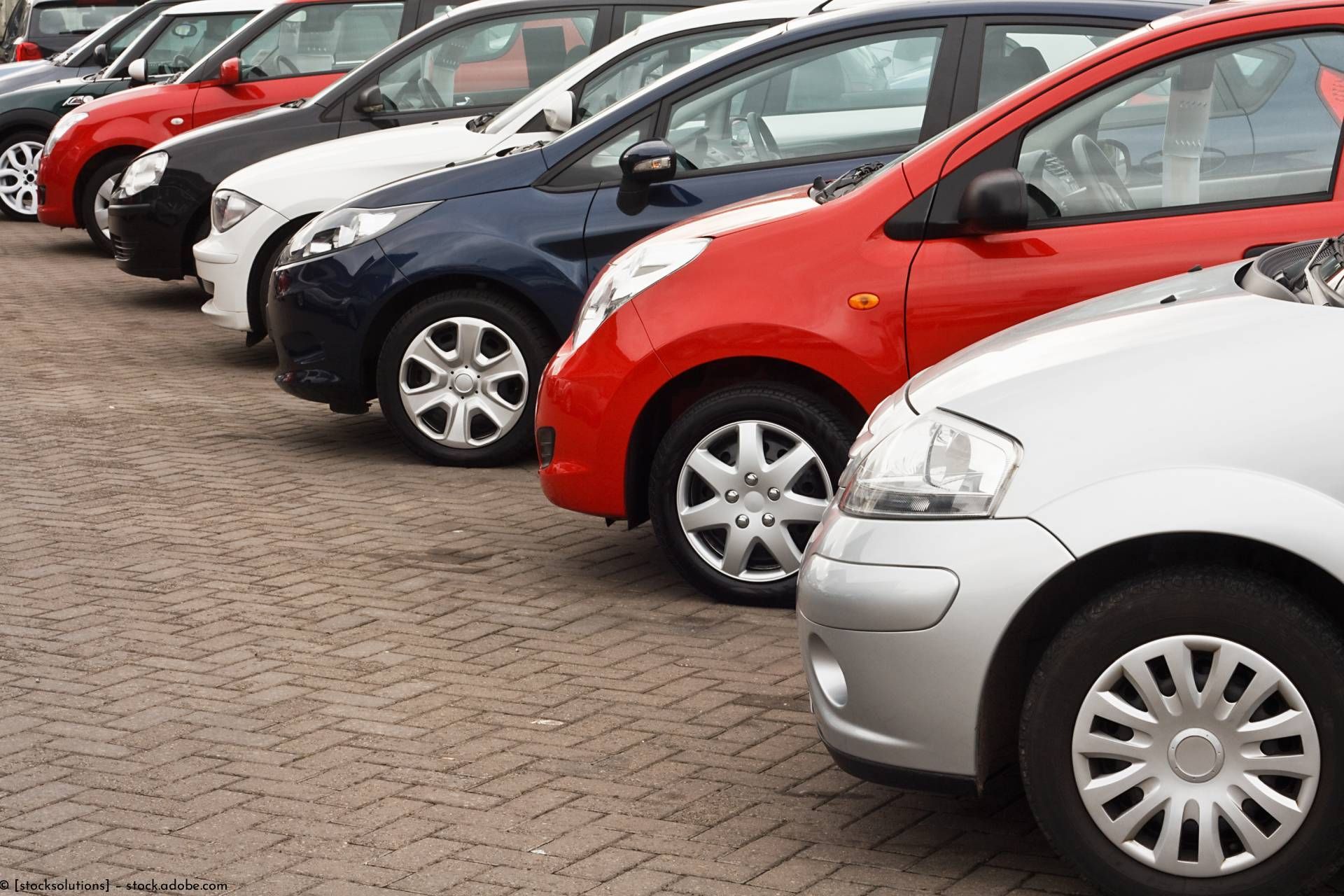 Eine Reihe geparkter Autos in verschiedenen Farben auf einem gepflasterten Parkplatz