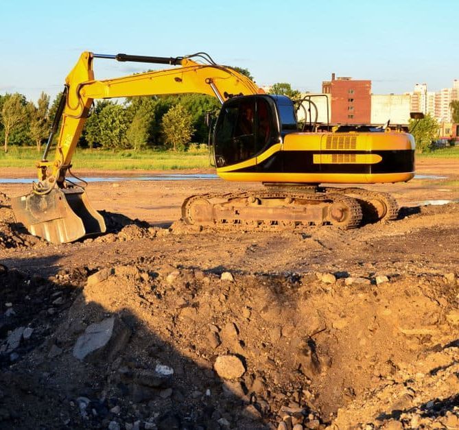Una excavadora amarilla está cavando un hoyo en un campo de tierra.