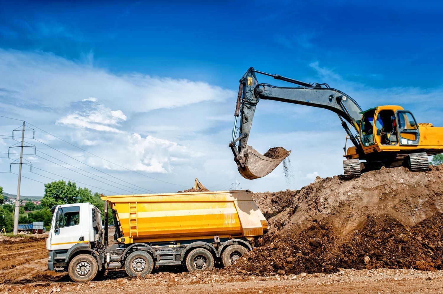 Una excavadora está cargando tierra en un camión volquete en un sitio de construcción.