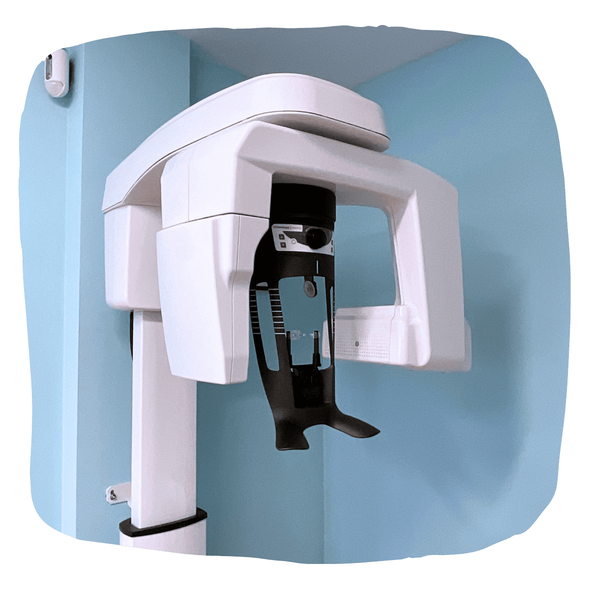 Máquina de rayos X panorámicos dentales, blanca y negra, contra una pared azul claro en el consultorio de un dentista.