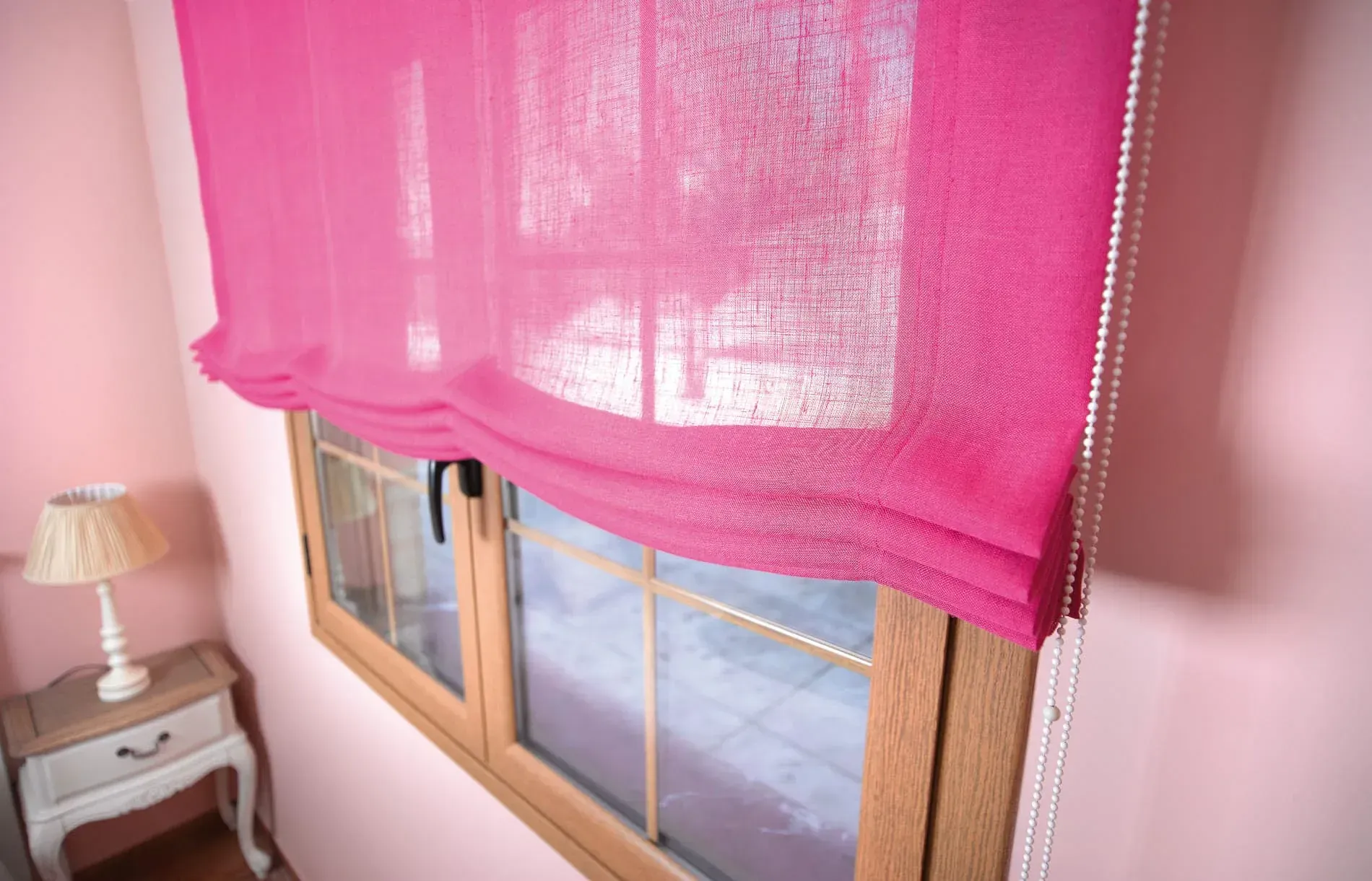 Una cortina romana de color rosa está colgada en una ventana de un dormitorio.