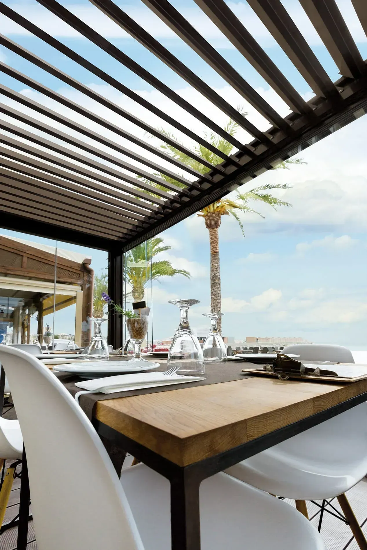 Una mesa y sillas bajo una pérgola con una palmera al fondo.