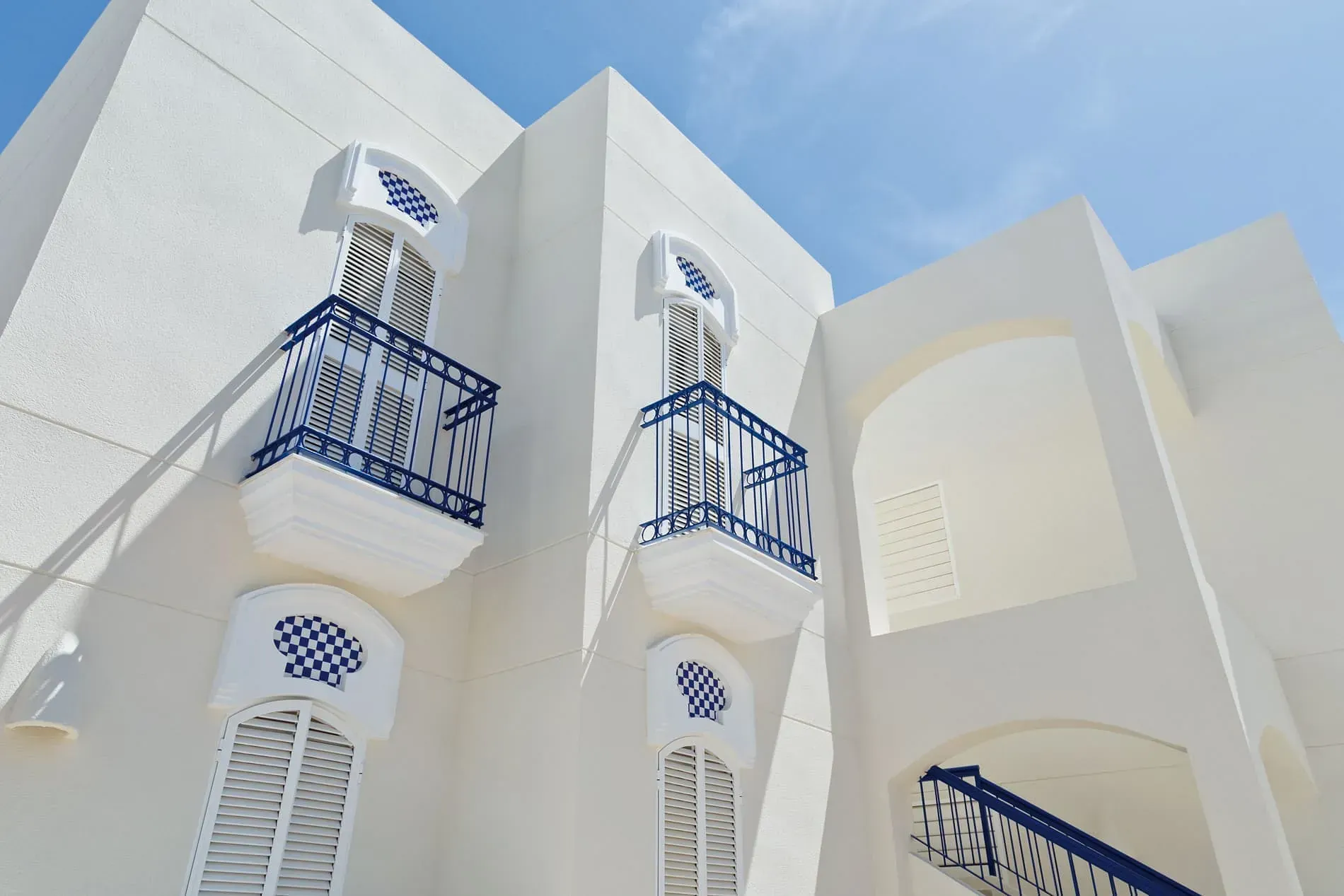 Un edificio blanco con balcones azules contra un cielo azul.