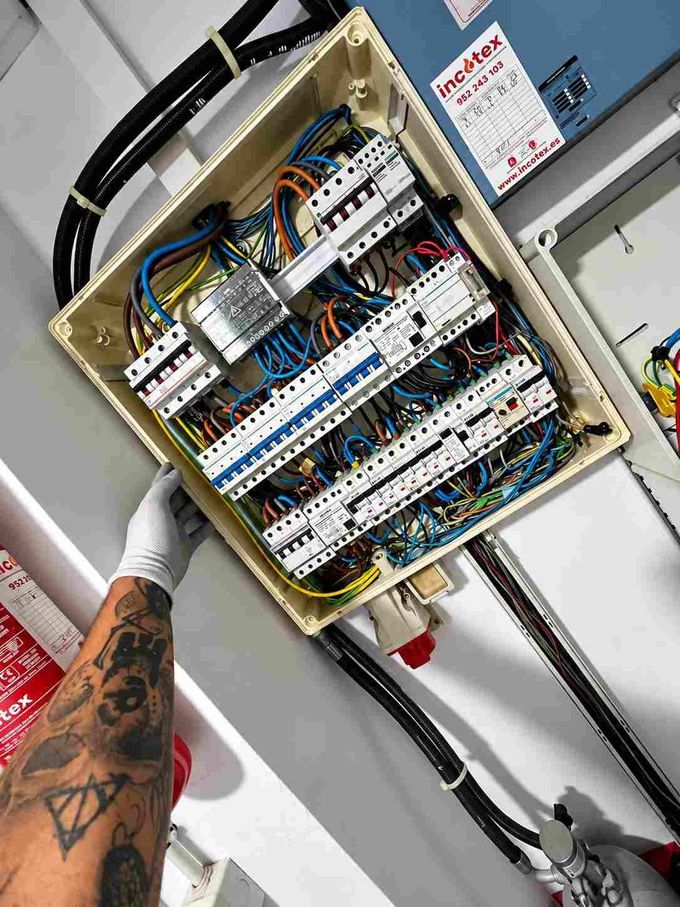 Mano enguantada trabajando dentro de un panel de control eléctrico