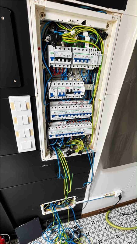 Panel eléctrico abierto con disyuntores, cableado y cables expuestos en un hueco de la pared.
