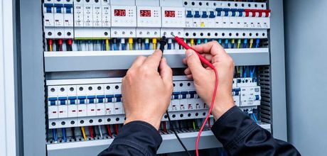 Manos probando un panel eléctrico con una sonda roja y cables negros.