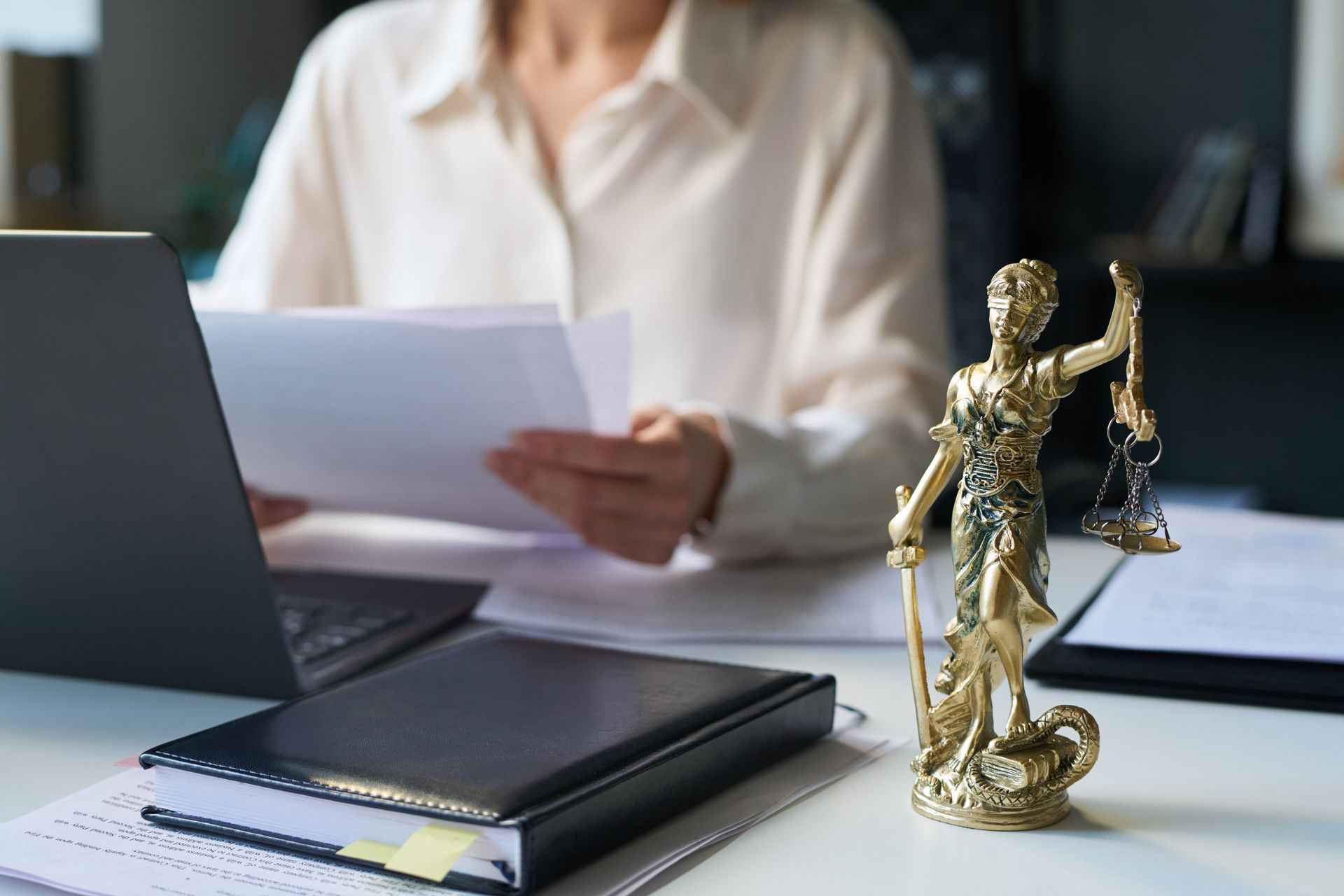 Bureau avec statue juridique, carnet, ordinateur portable et personne examinant des documents dans un bureau