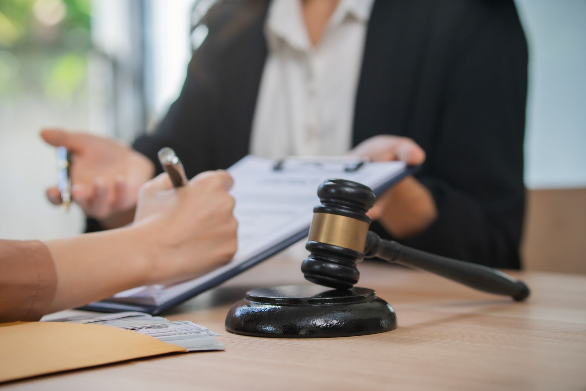 Un avocat et son client signent des documents à côté du marteau d'un juge, sur un bureau.