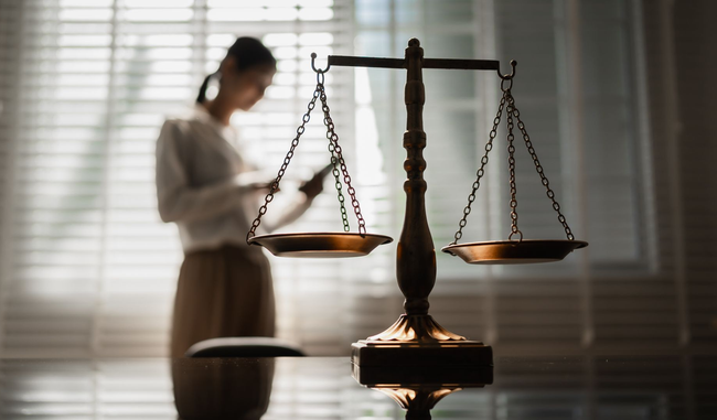 Une balance de la justice sur un bureau, avec un avocat flou en arrière-plan près d'une fenêtre