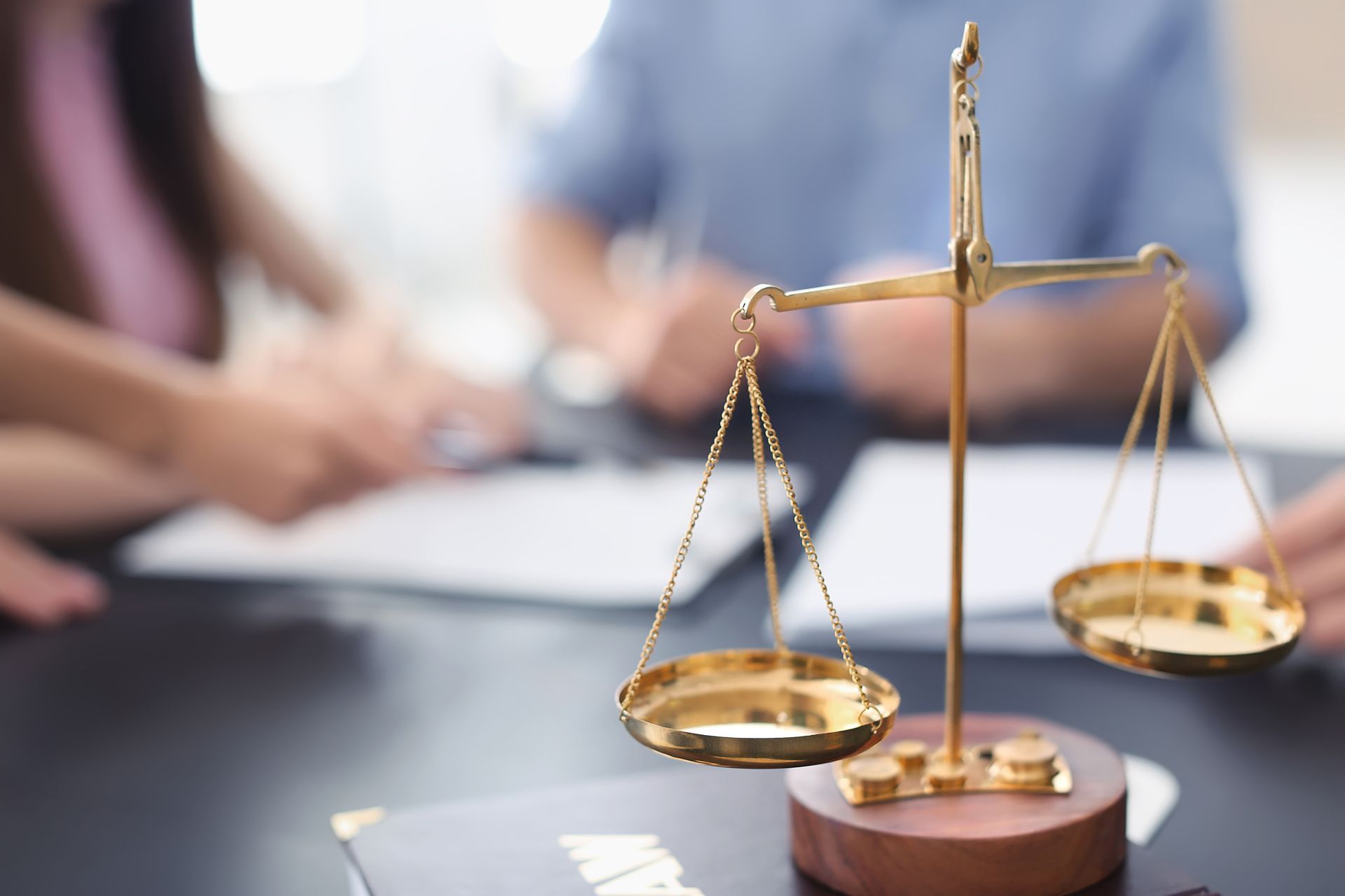 Une balance en laiton, symbole de la justice, posée sur un bureau, avec des personnes floues travaillant en arrière-plan.