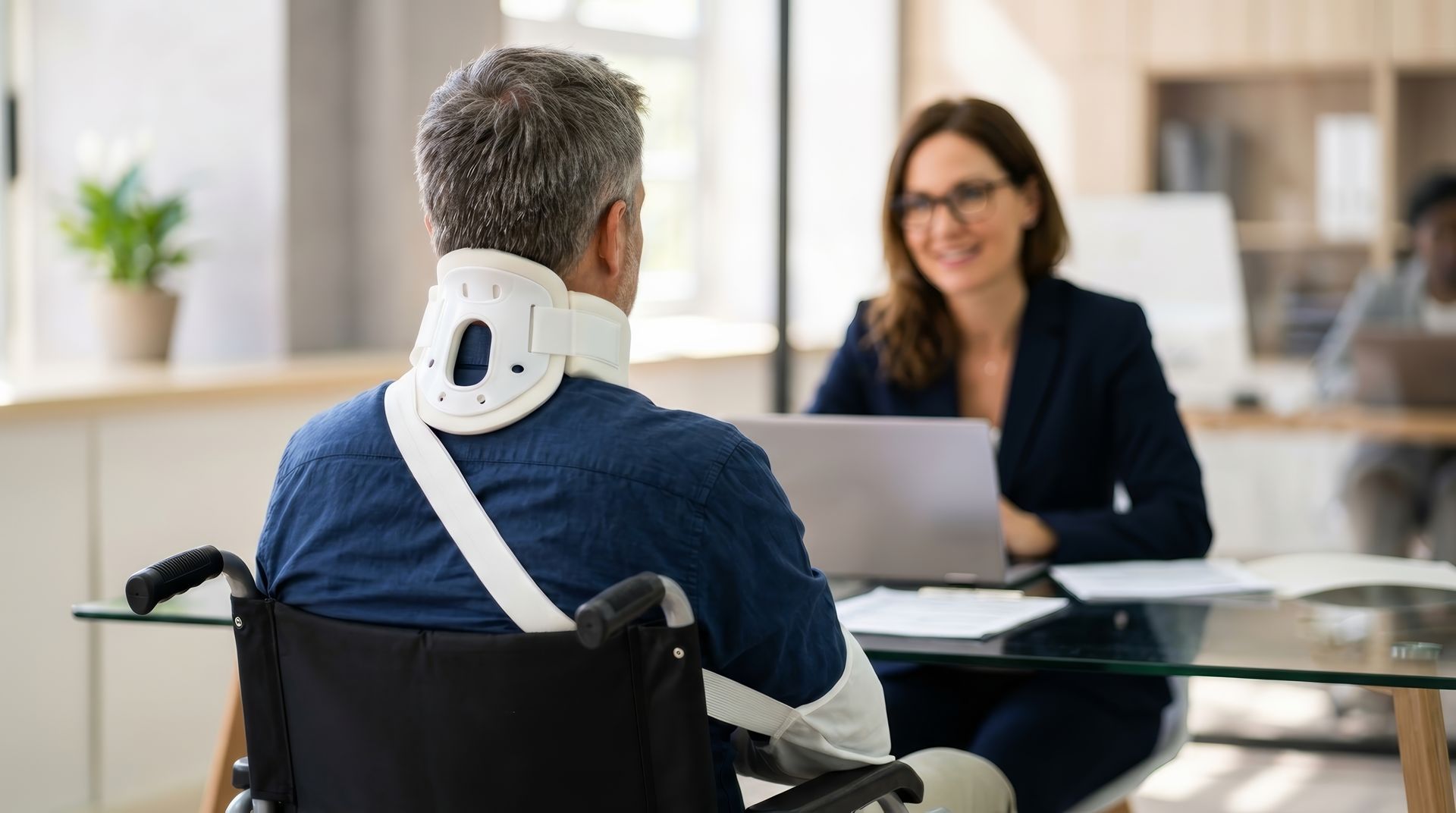 Une personne en fauteuil roulant discute avec une femme souriante assise de l'autre côté d'un bureau dans un bureau lumineux.
